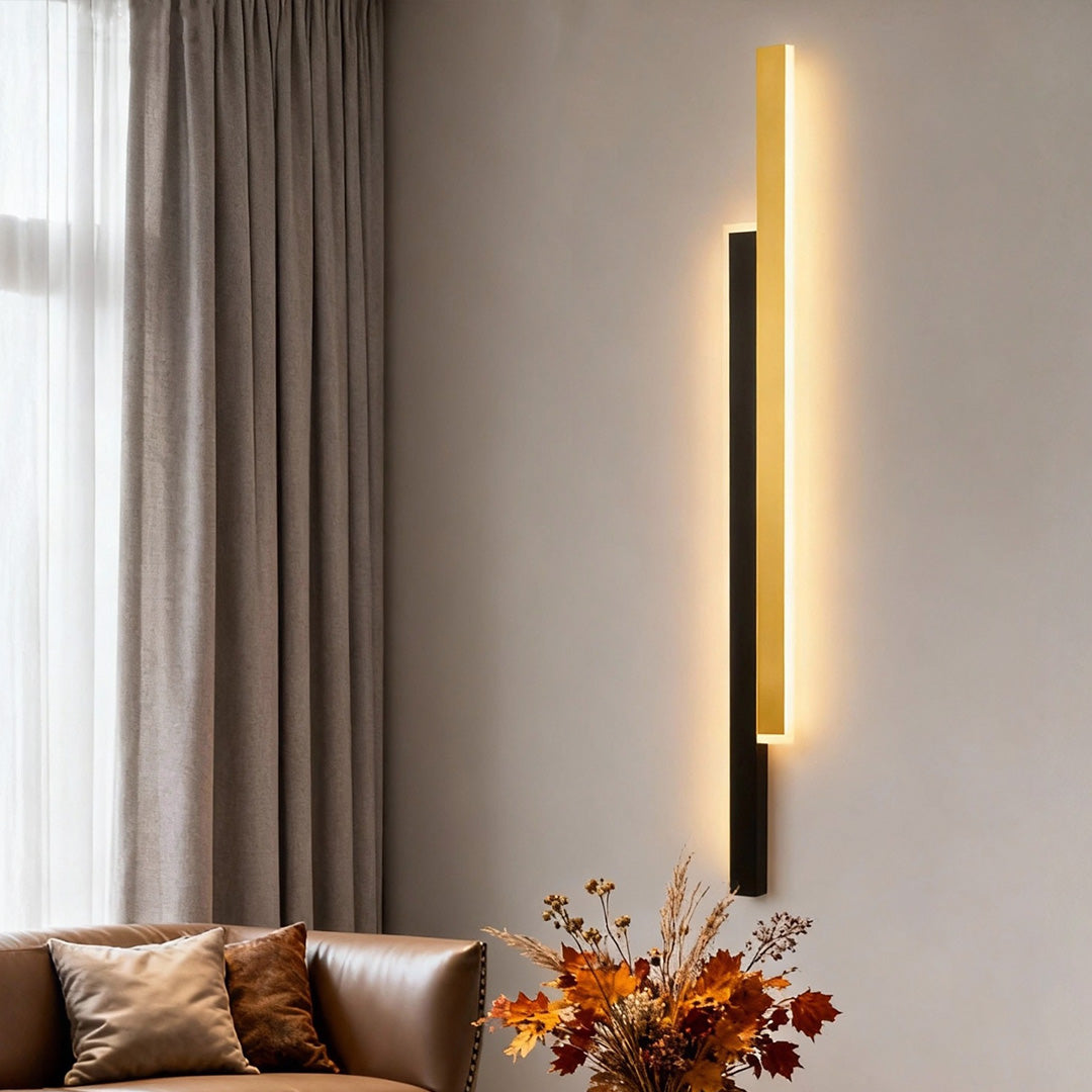 Sleek vertical wall light with gold and black finish mounted beside curtains in modern living room setting.