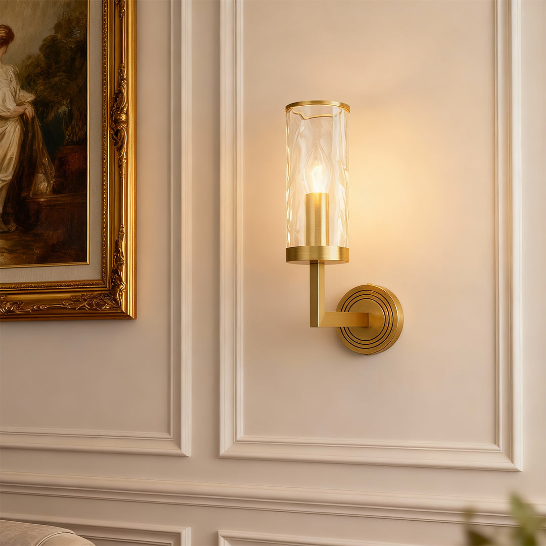 Wall glass light illuminating elegant hallway with paneled walls and gold-framed artwork.