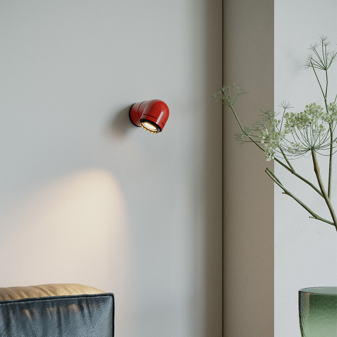 Red wall modern lights illuminating a soft neutral wall in a cozy bedroom corner.