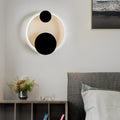 Wall mounted nightstand lights with circular backlit design and black accents, creating a soft ambient glow above a modern bedside table.