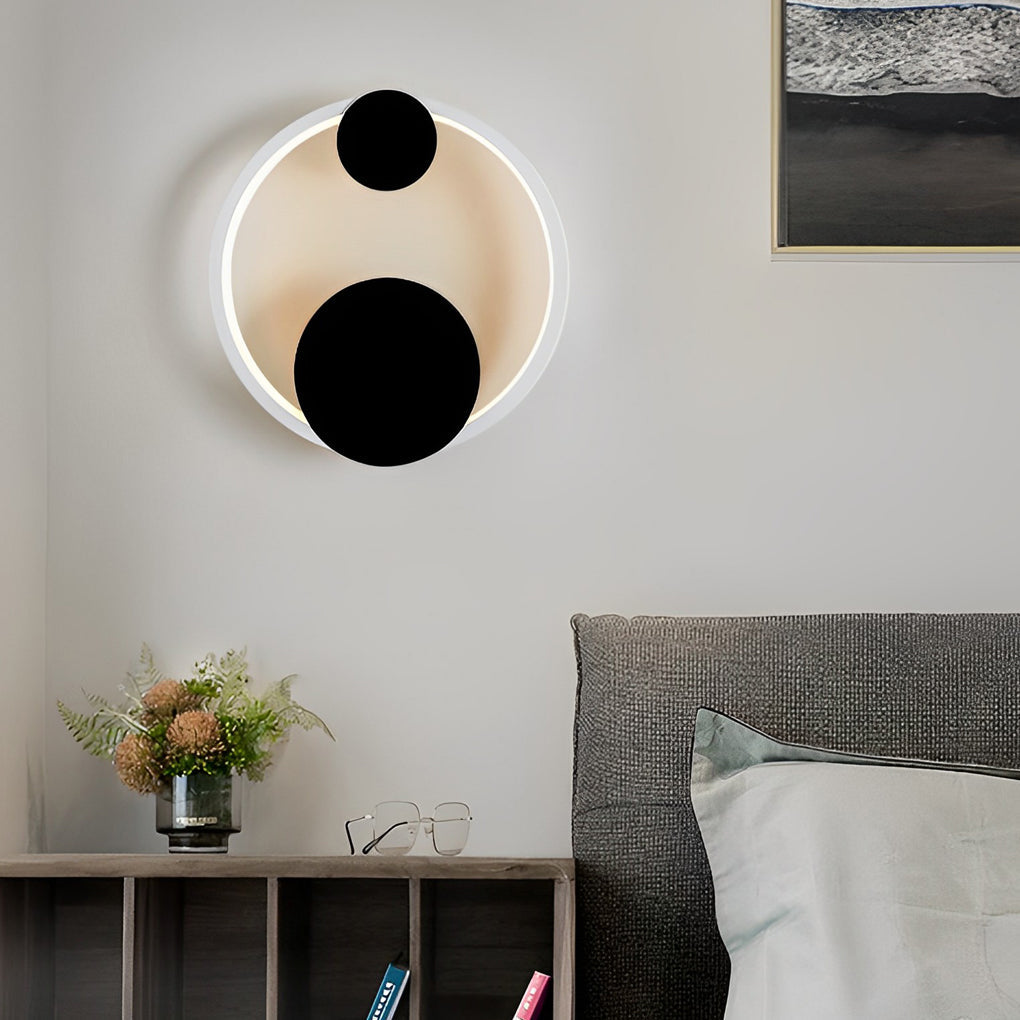 Wall mounted nightstand lights with circular backlit design and black accents, creating a soft ambient glow above a modern bedside table.