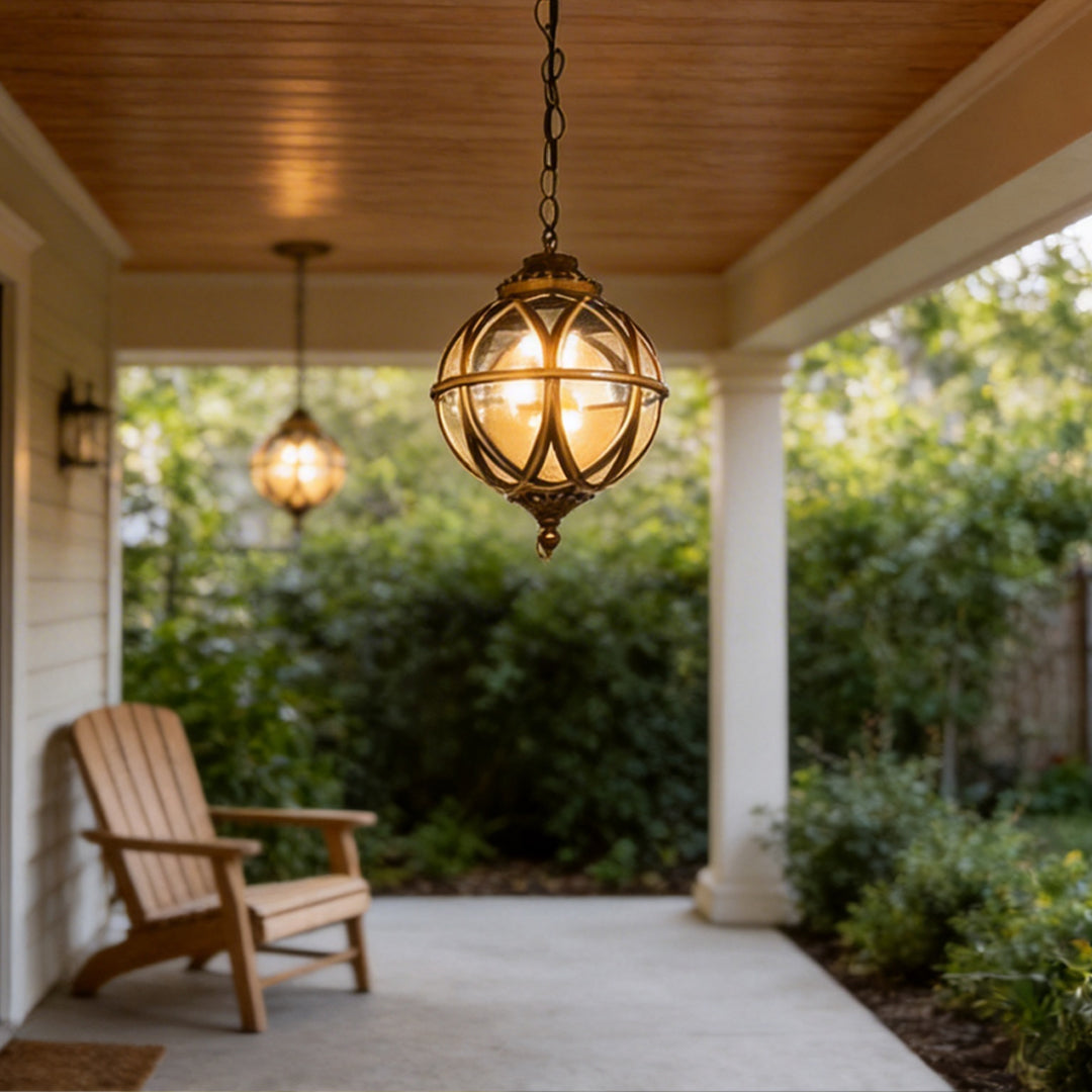 Warm glowing metal orb pendant light illuminating a cozy outdoor porch with a wooden chair now.