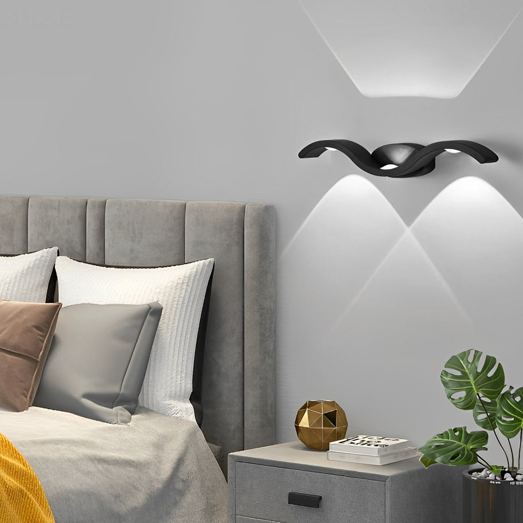 Black wave wall sconce installed outdoors, illuminating a garden wall with elegant upward and downward beams.